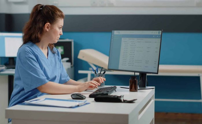 Nurse typing on computer keyboard for consultation and appointment. Medical assistant using technology for healthcare system in doctors office. Specialist working with medical equipment